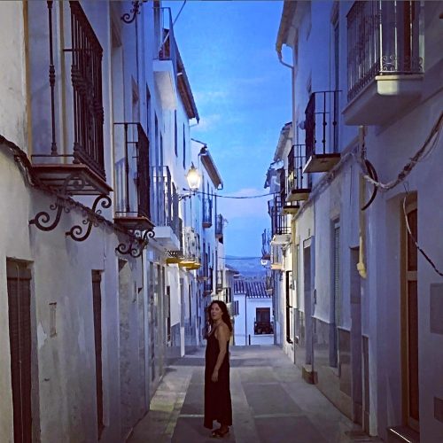 Viil wearing a black dress in an atmospheric old street at dusk.